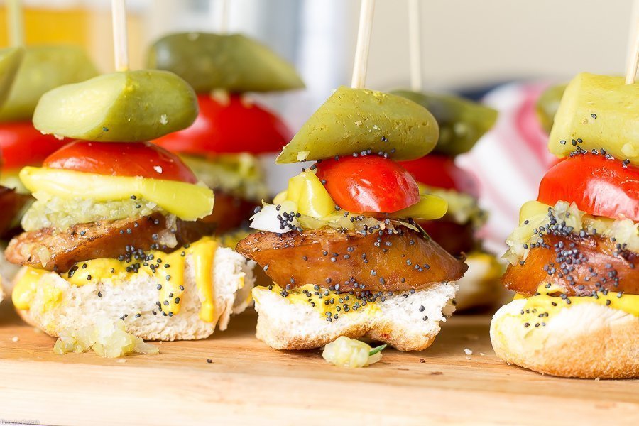 pan tostado, rebanada gruesa de salchicha ahumada, condimento dulce, cebolla blanca, mostaza amarilla, lanza de pepinillo, semillas de sésamo, todo en un bocado en un pincho, primer plano horizontal