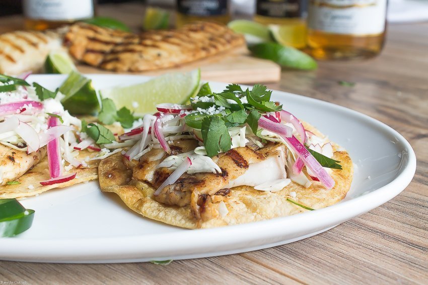 Tacos de pescado a la parrilla marinados con cerveza, estos tacos clásicos están cubiertos con repollo rallado, rábanos, cebollas rojas en escabeche, rodajas de jalapeño y queso cojita.