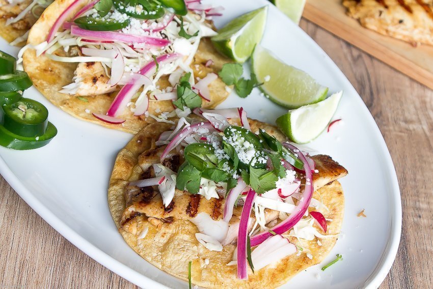 Tacos de pescado a la parrilla marinados con cerveza, estos tacos clásicos están cubiertos con repollo rallado, rábanos, cebollas rojas en escabeche, rodajas de jalapeño y queso cojita.